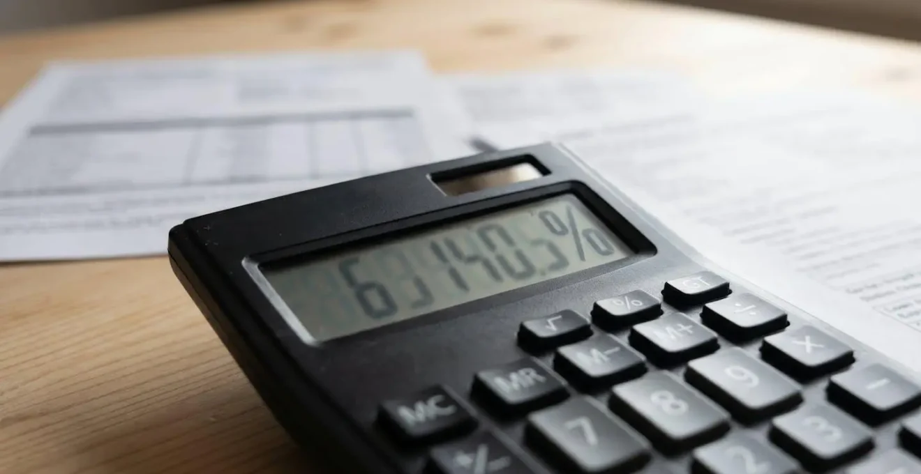 Gros plan d'une calculatrice moderne affichant un pourcentage sur un bureau en bois clair avec des documents floutés en arrière-plan